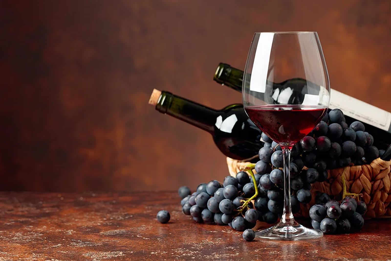 Copa de malbec junto a botellas y racimos